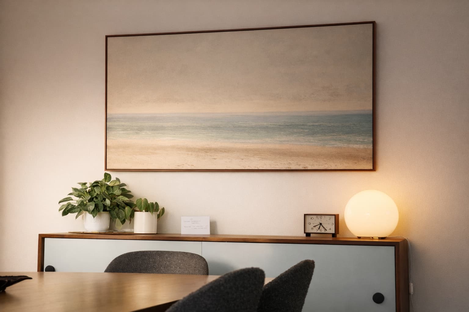 Framed seascape above a walnut credenza with plants and a glowing globe lamp