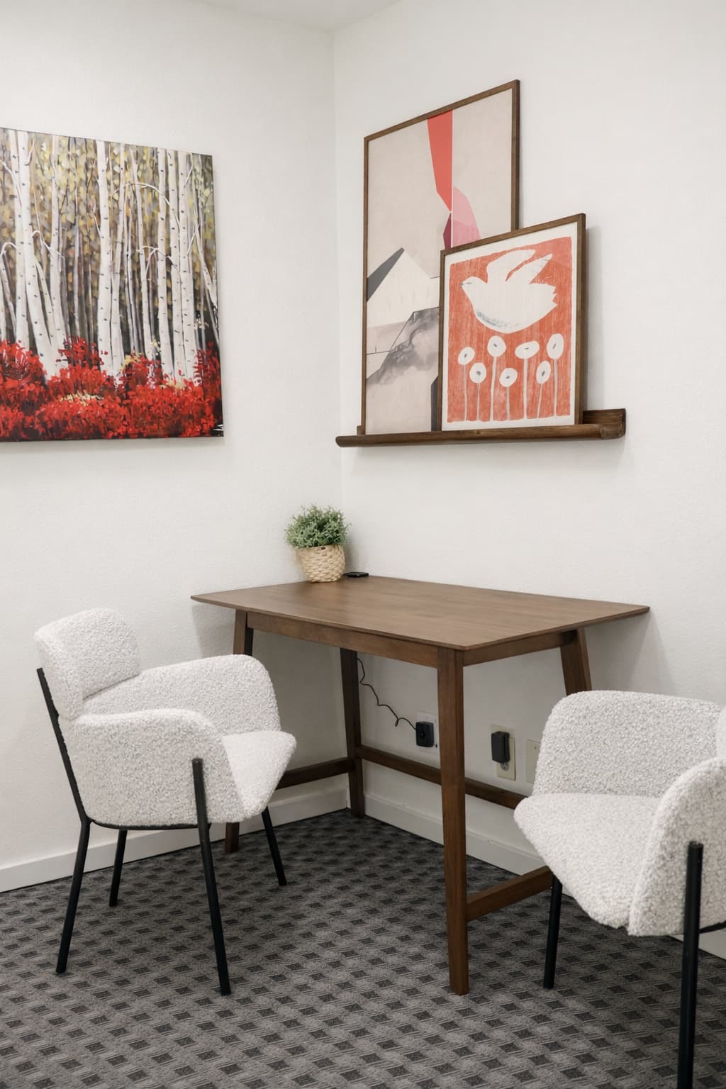 Work nook with white boucle armchairs, a walnut desk, and a red birch-forest painting